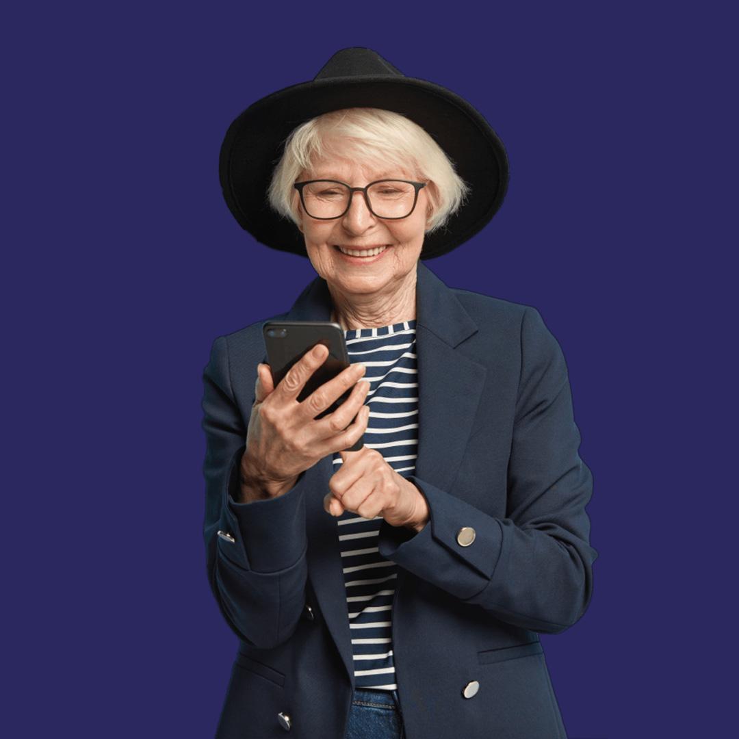 An older woman wearing a black hat, striped top and navy blazer smiles as she looks at her mobile phone.