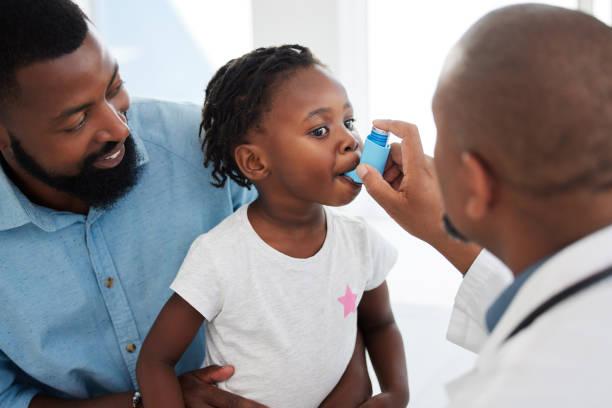 photograph of a father and young daugher and a doctor. The father is holding the child on his lap and smiling. The doctor is administering an asthma inhaler to the child.