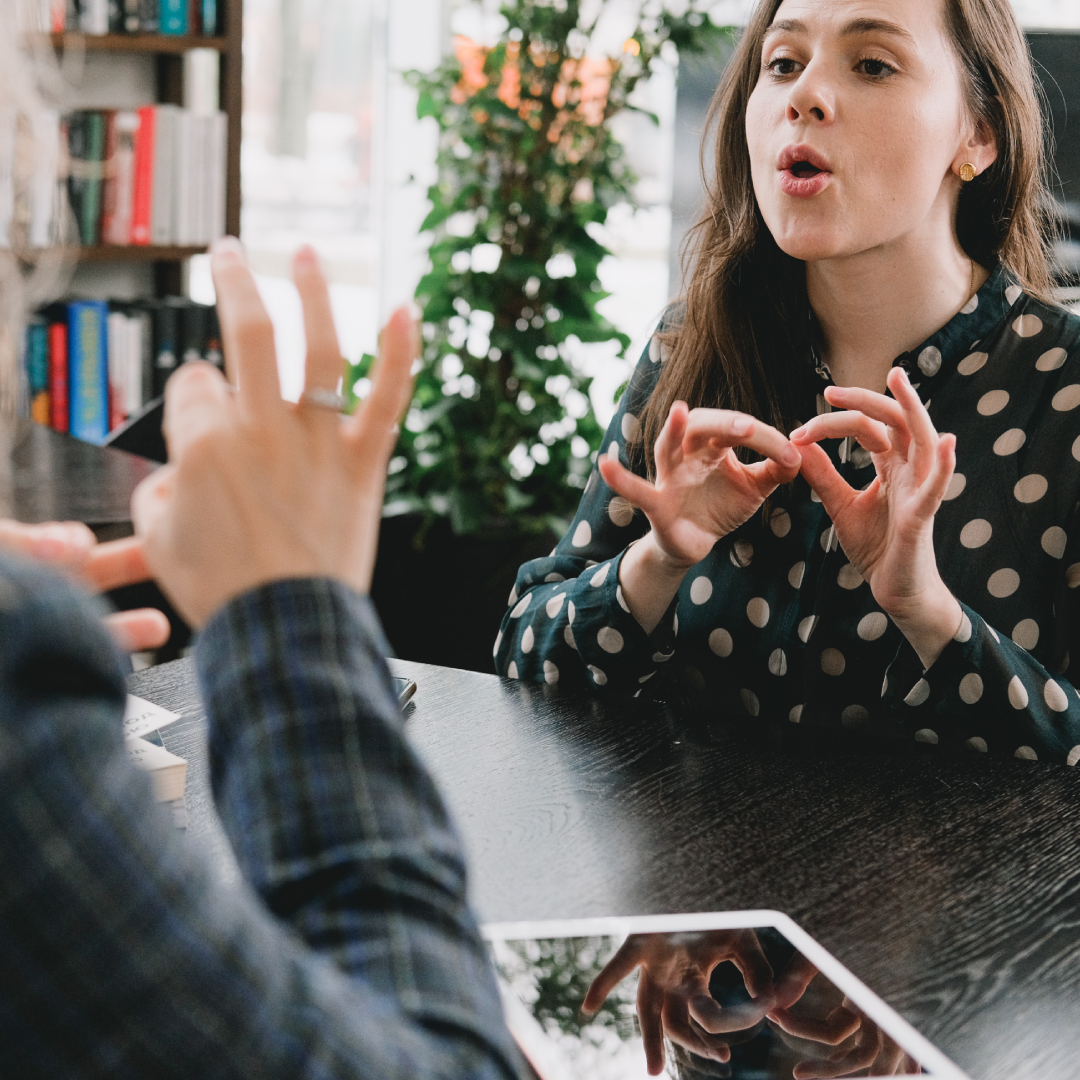 Young girl communicating through sign language with another person. the second person has their back to the shot.