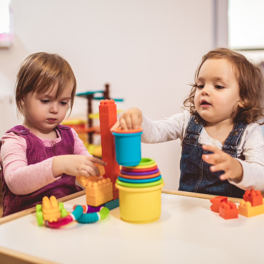 Two children playing. They are stacking blocks one of top of the other.