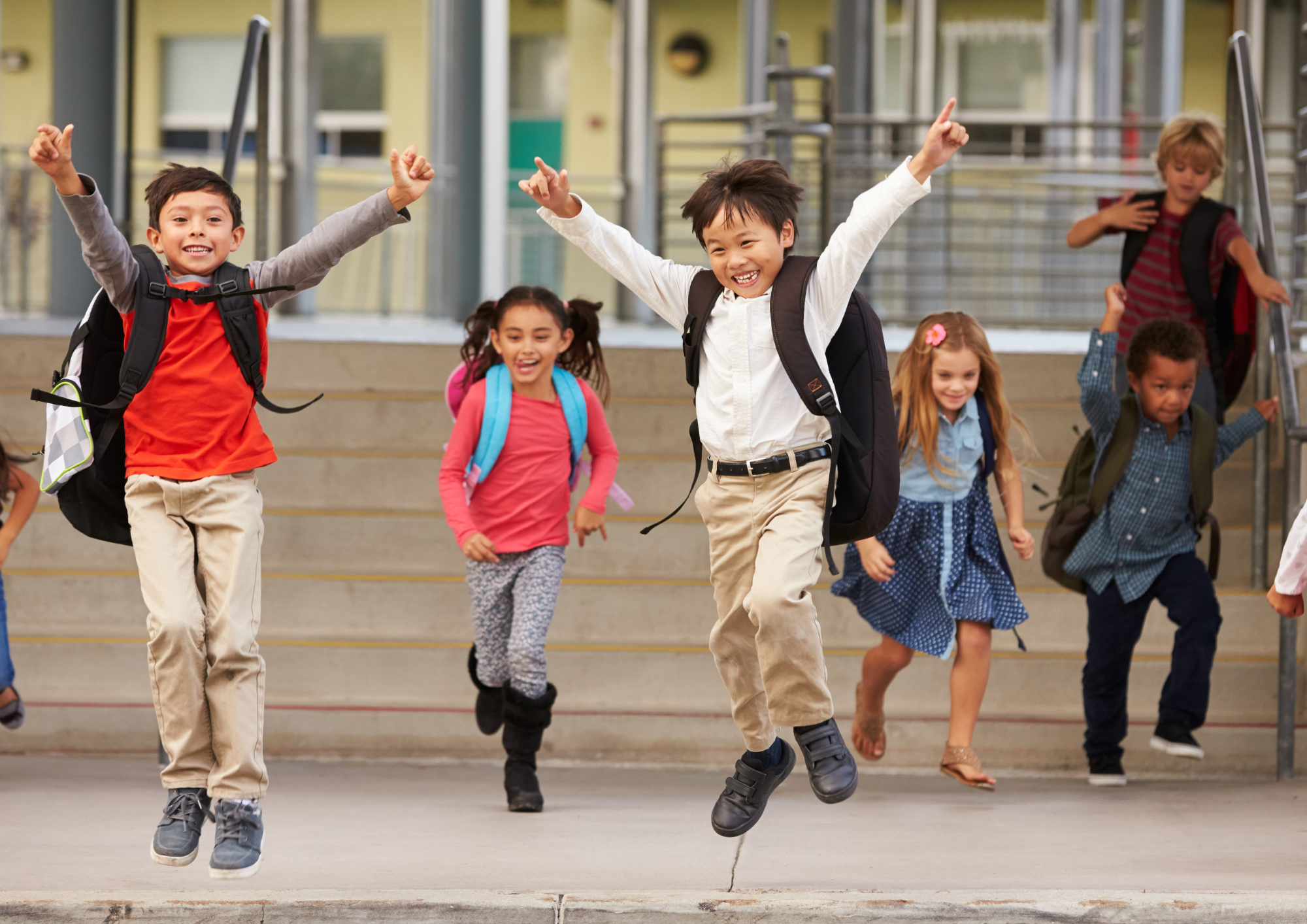 A group of children in school uniforms and backpacks happily hopping at the school gates