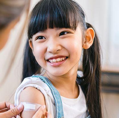 A young girl smiling as a plaster is applied after a vaccination.