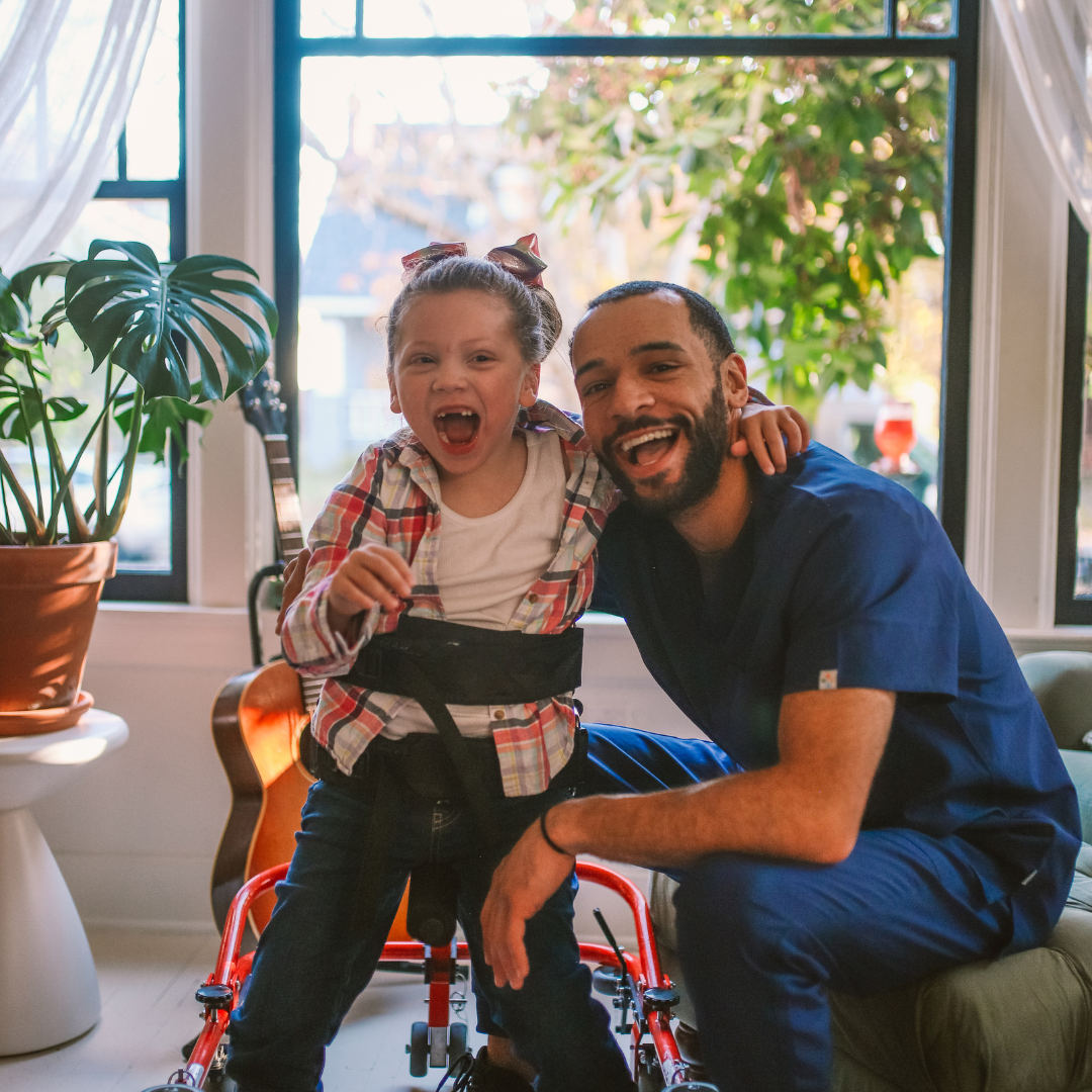 An adult and child next to each other smiling at the camera. The child has his hip and legs attached to a walking supportive equipment.