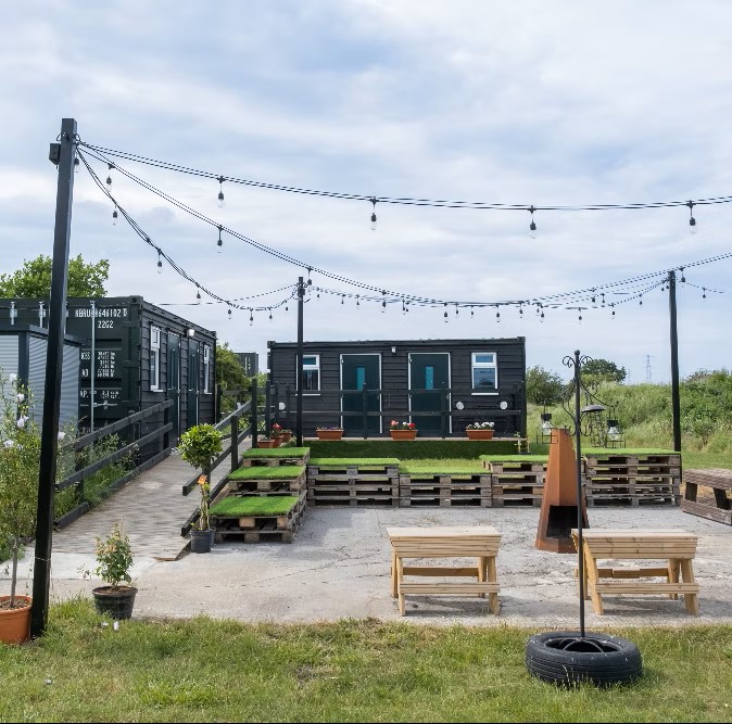 A photograph of the Pods at Time and Space. The picture shows 2 converted black shipping containers set in an attractive outdoor area.