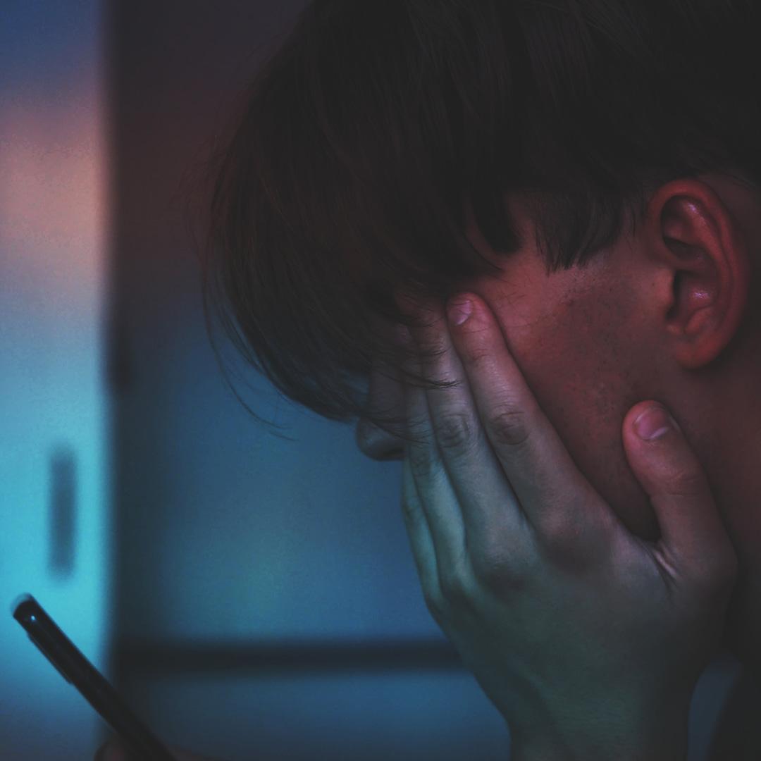 Male teenager with his head in his hands whilst looking at his smartphone