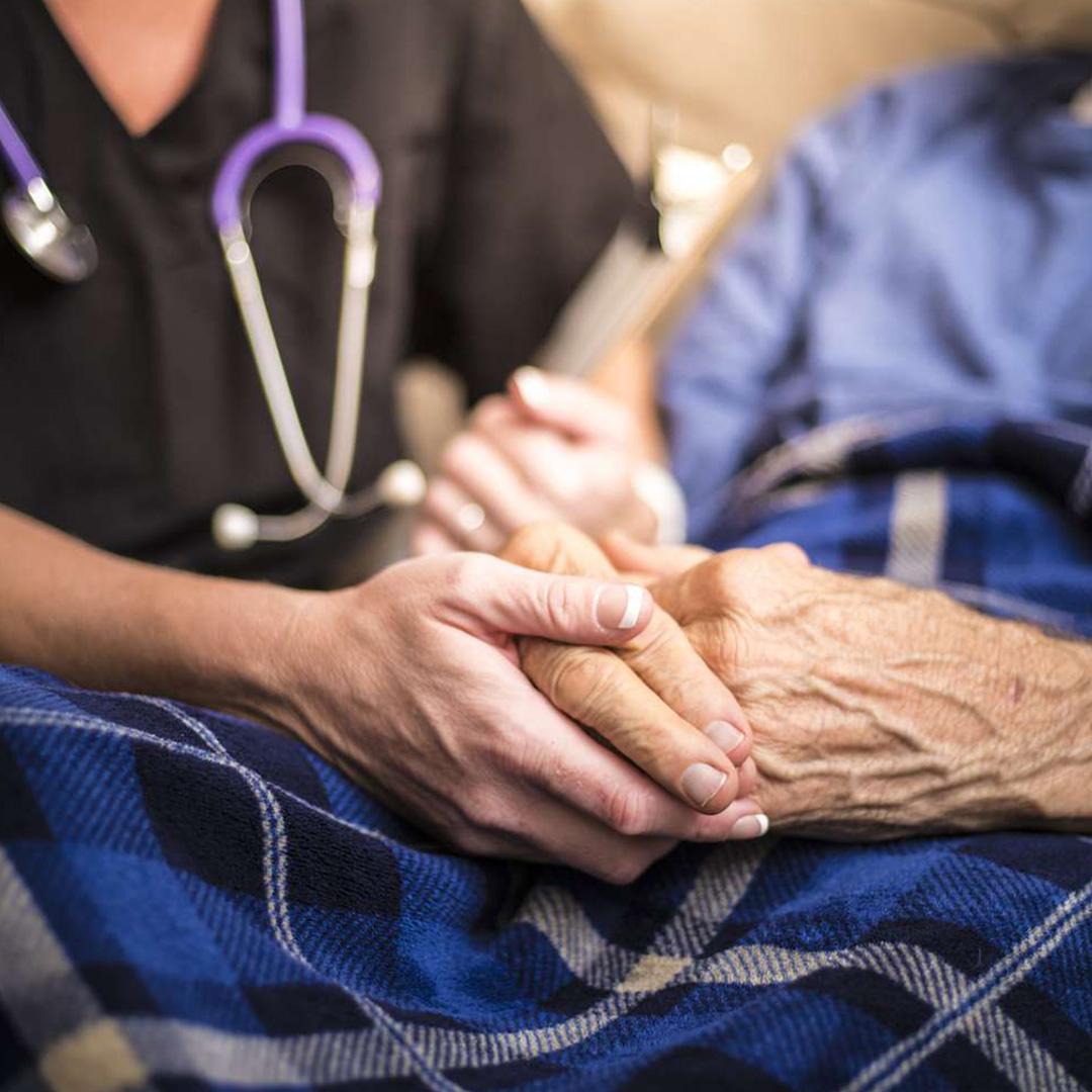 A nurse holds an elderly woman's hands in close up.