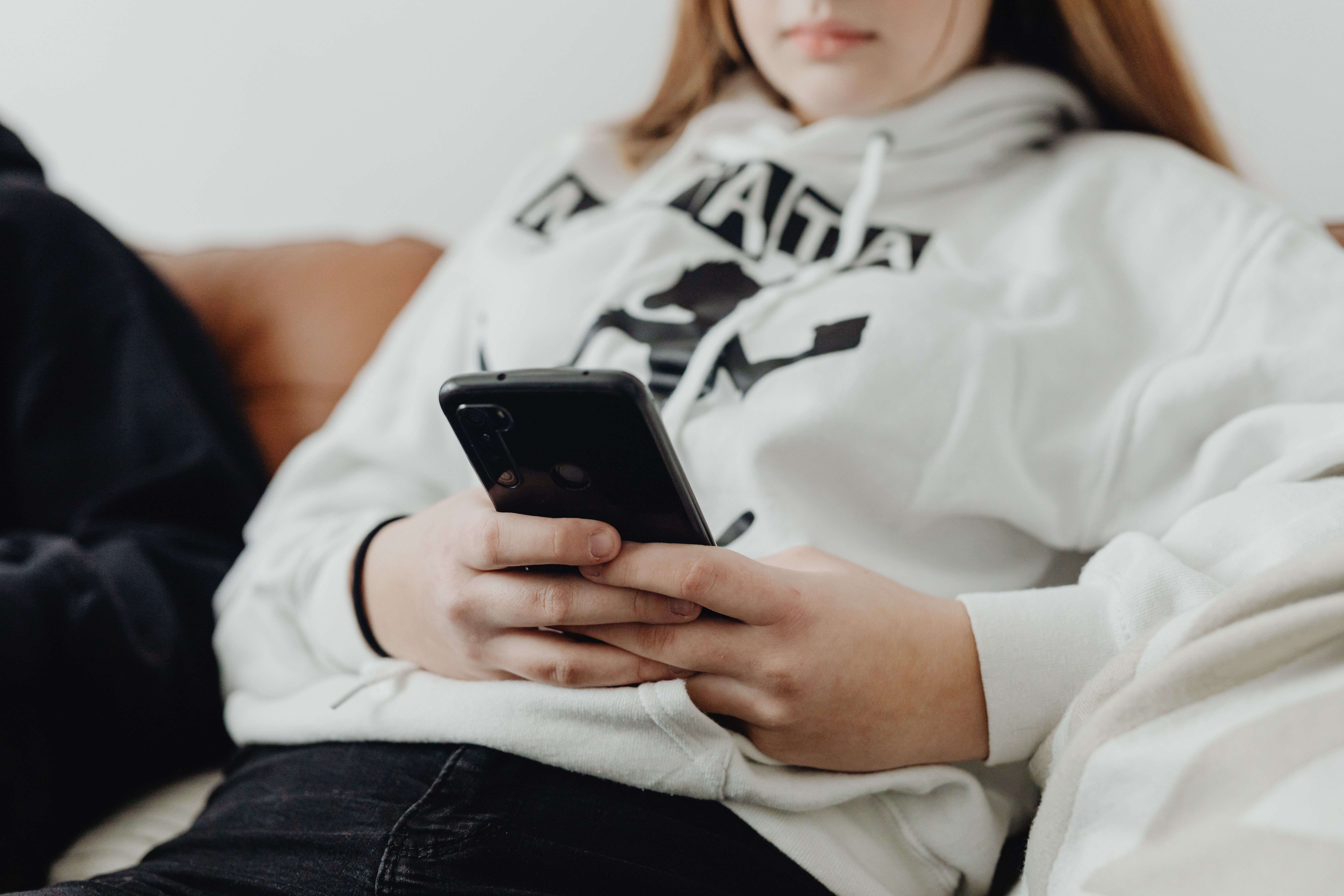 A teenage girl in a white hoodie using a smartphone.