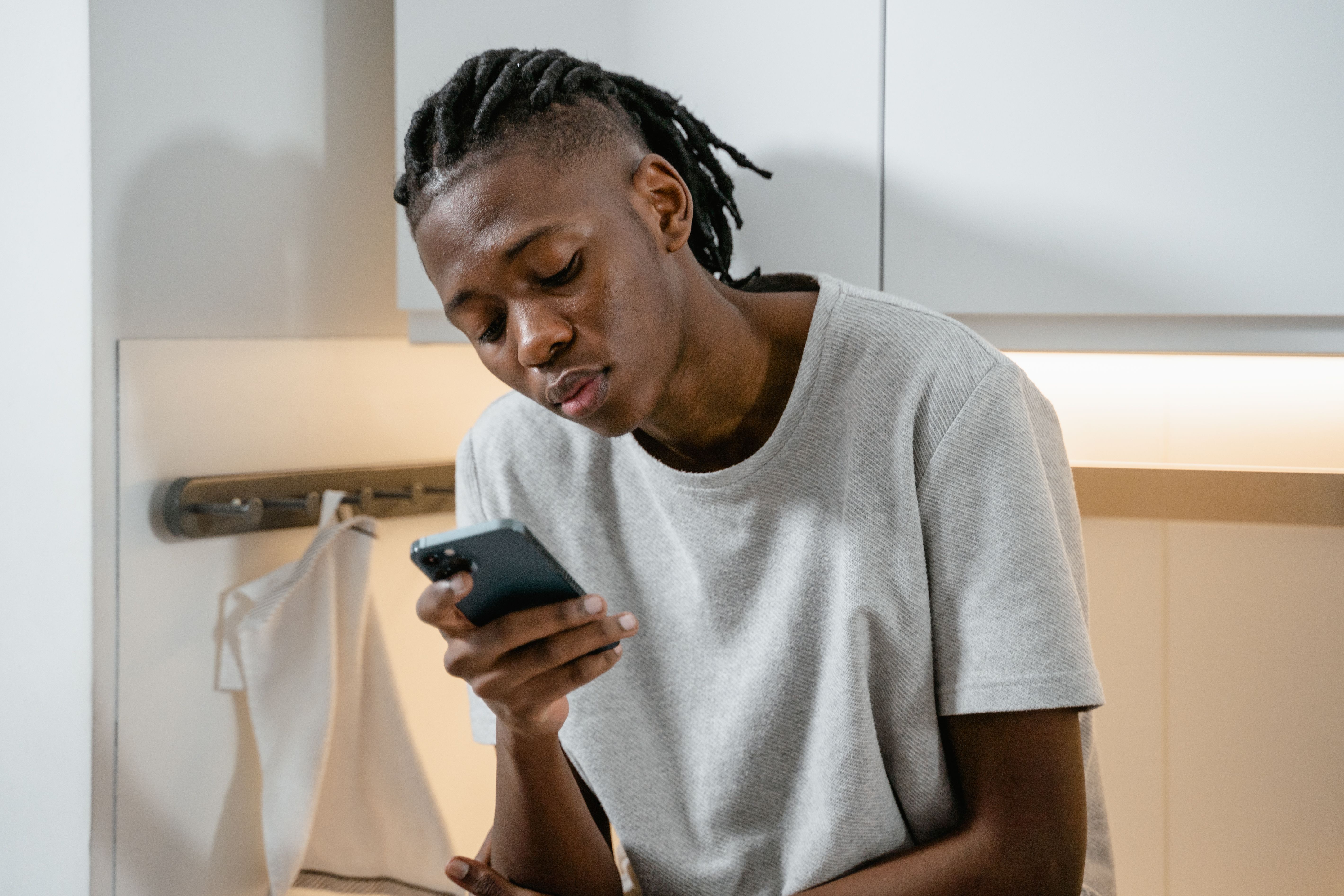 Focused individual texting on smartphone in modern kitchen environment.