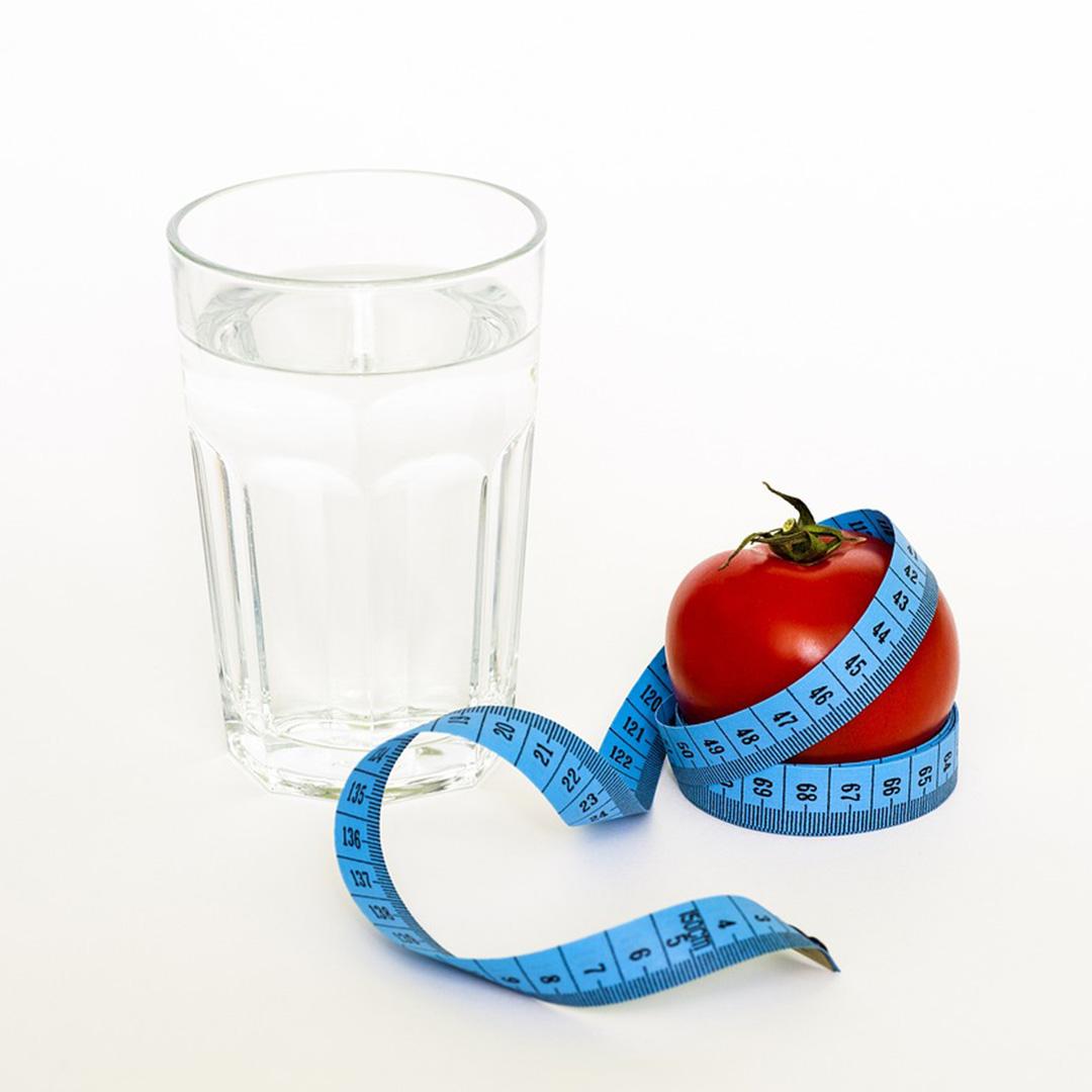 a glass of water, a blue measuring tape and a red apple